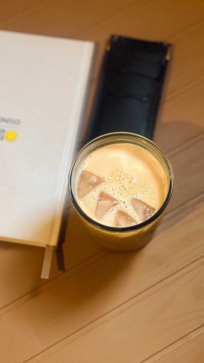 Refreshing iced coffee next to an open book on a wooden table, perfect for a cozy reading session.