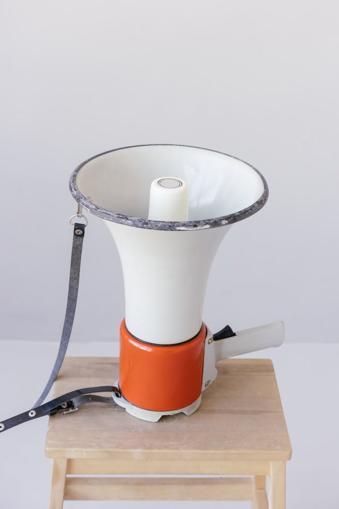 A classic megaphone rests on a simple wooden stool with neutral background.